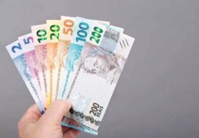 Pessoa segurando cédulas de real brasileiro de diferentes valores, representando organização financeira, economia e planejamento para guardar dinheiro com data para retirar.